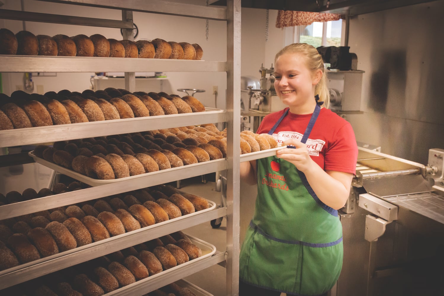 Baker smiling with trays of fresh donuts.