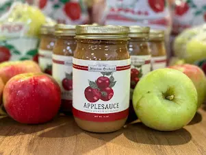 Jars of applesauce with fresh apples on display.