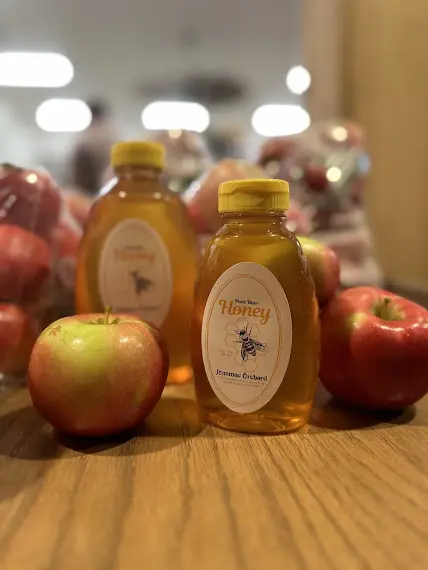 Bottled honey with red apples on wooden table.