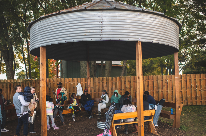 Group sitting under a metal gazebo in park.