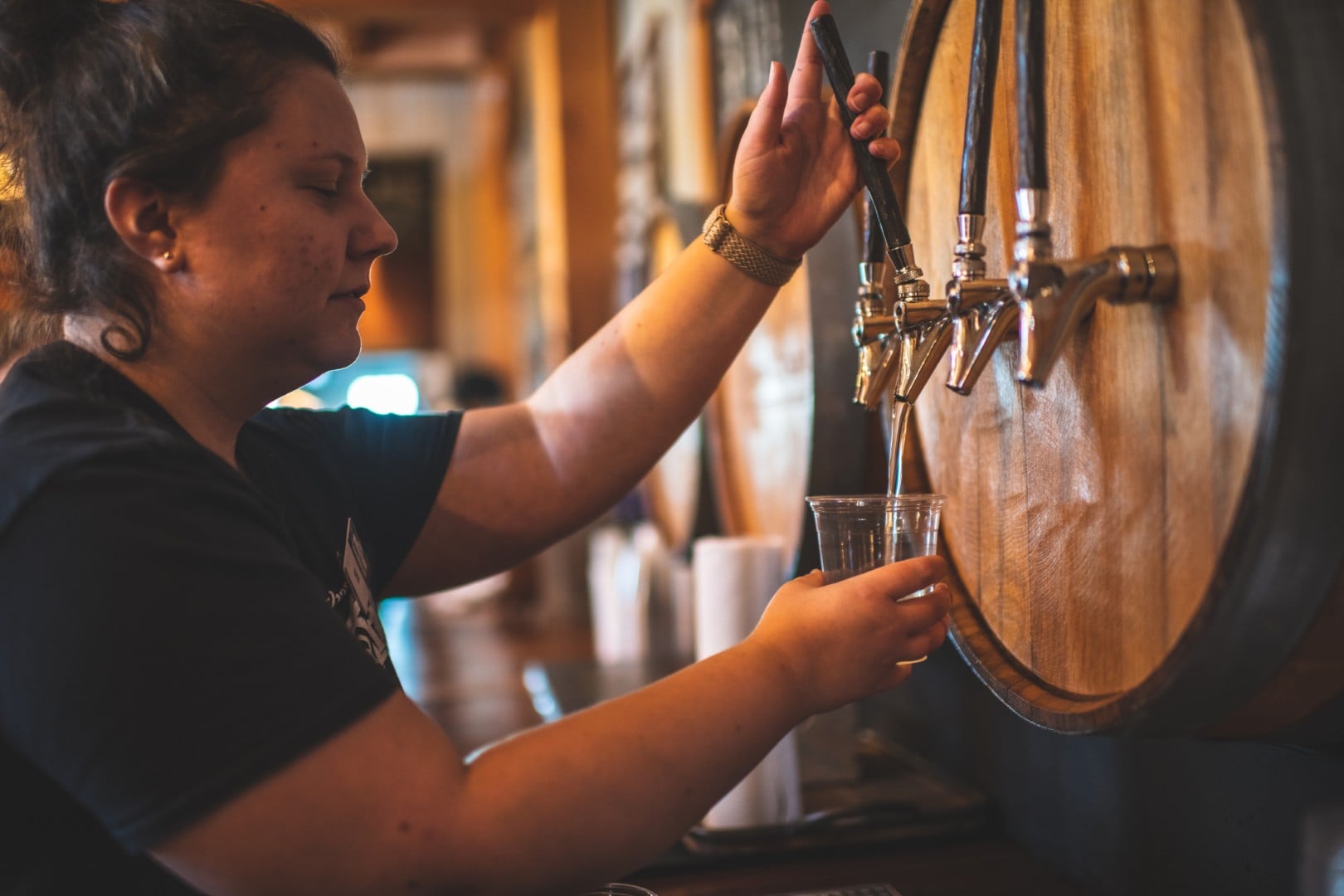Person pouring drink from barrel tap in brewery.