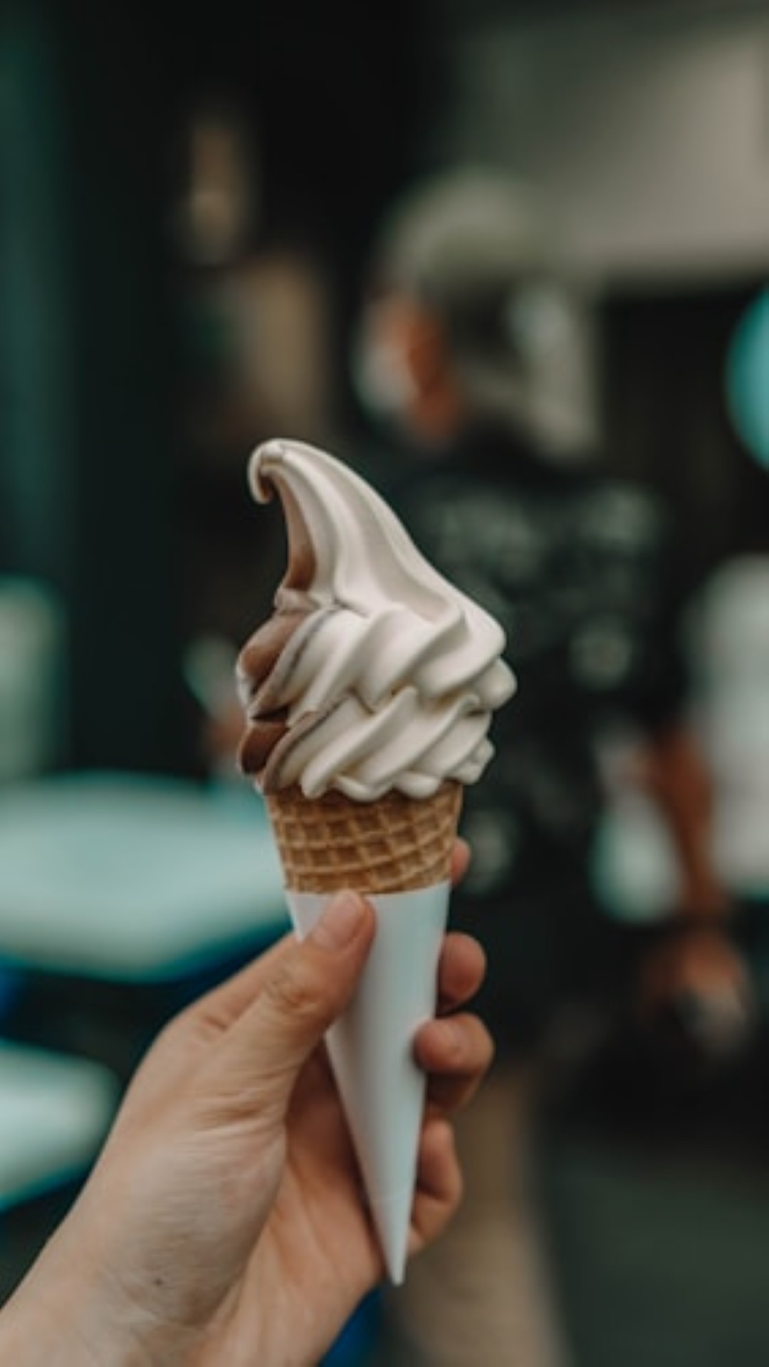 Hand holding vanilla-chocolate swirl ice cream cone.