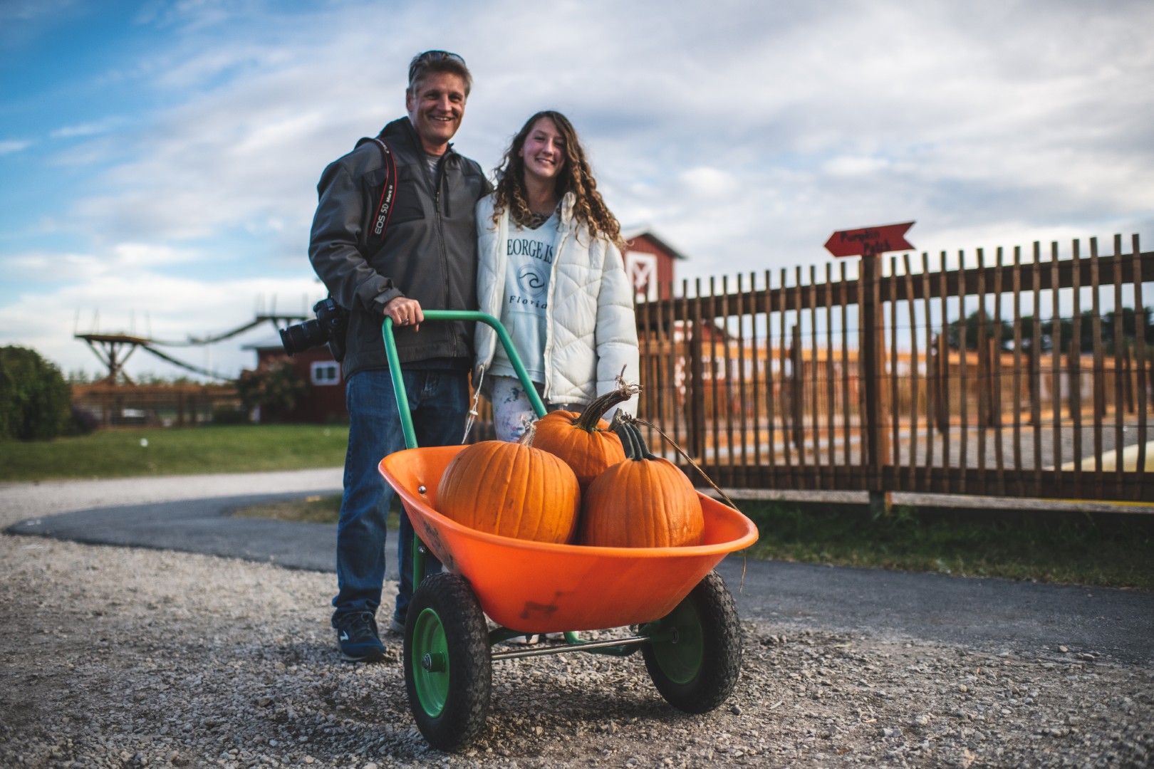 Two people with wheelbarrow of pumpkins at farm.